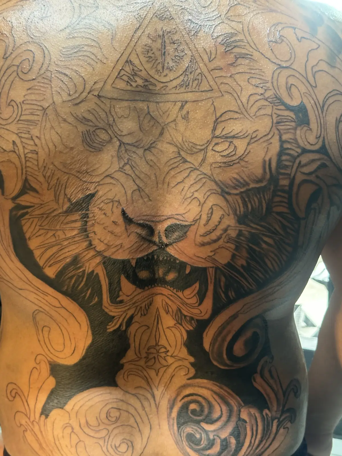 Tatuagem de leão em preto e cinza nas costas, realismo monocromático