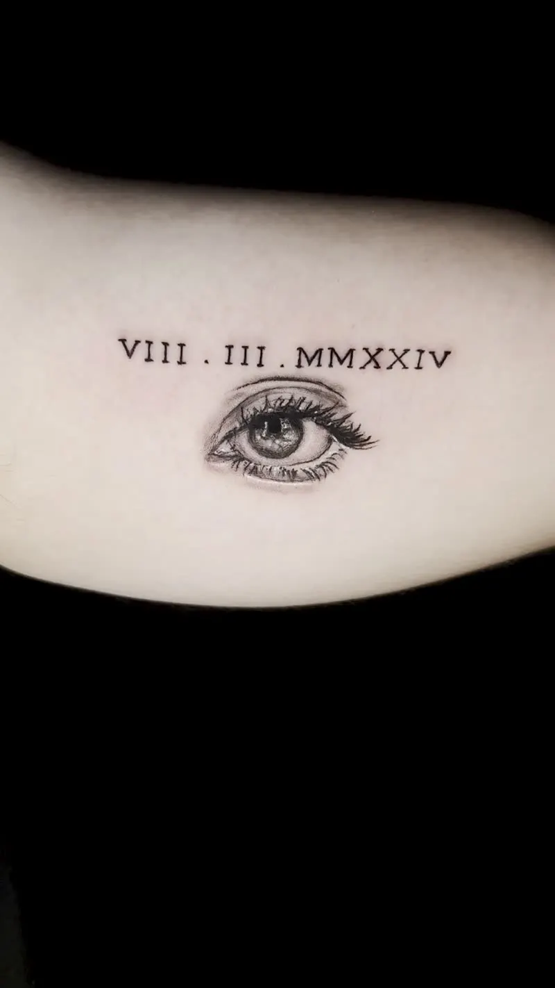 Tatuagem realista de olho com data romana no braço feita em Cuiabá